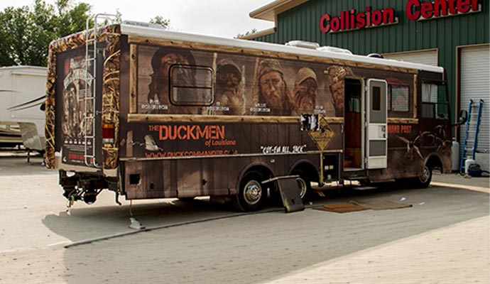Large RV with custom graphic wrap parked outside collision center building