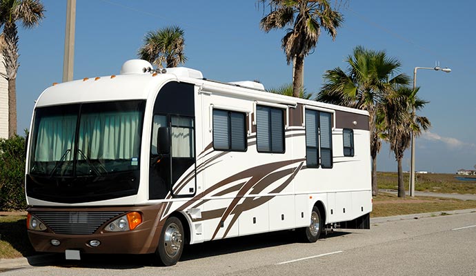 Large motorhome parked on roadside with palm trees in background