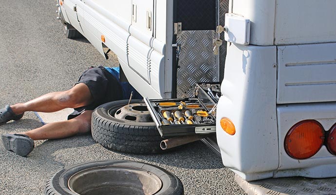 Technician performing on-site RV repairs from beneath the vehicle