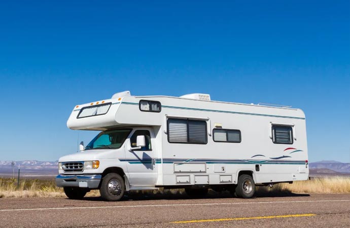 A white RV drives on a desert road.