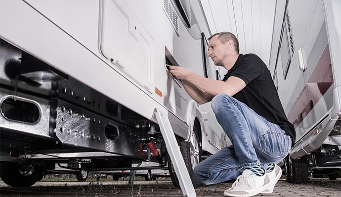 Technician kneeling beside RV repairing exterior access panel